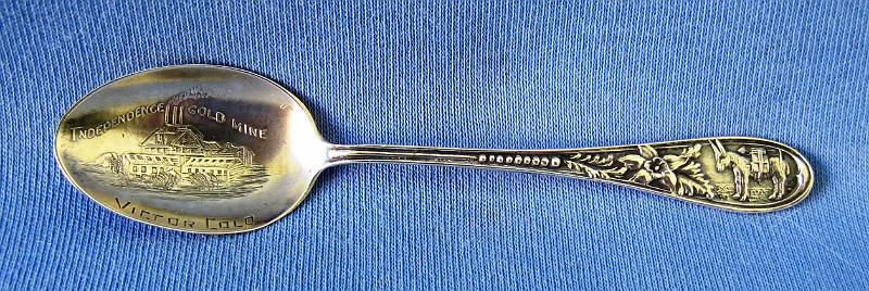 Souvenir Mining Spoon Independence Gold Mine.JPG - SOUVENIR MINING SPOON INDEPENDENCE MINE - Sterling silver spoon embossedwith a detailed picture of the Independence Gold Mine Victor Colo; handle decorated with a miner’s donkey at top and floral pattern front and back, 3 1/2 in. long, weight 8 gms., marked on back Sterling  (W. S. Stratton's Independence Mine and Mill were located near Victor, Colorado on the south slope of Battle Mountain. In the spring of 1891 Stratton persuaded Leslie Popejoy to grubstake him in the Cripple Creek District in return for half the profits. Stratton staked two claims on the south slope of Battle Mountain on July 4, 1891. He called the two claims the Independence and the Washington in honor of the holiday. Assays from the Independence lode showed a value of $380 per ton gold so Stratton quickly sold his house and two lots, one in Denver and one in Colorado Springs, so that he could buy out Popejoy's share.   One boulder from the Independence Mine brought $60,000, which Stratton used to sink a chute. In doing so he tapped directly into a rich vein.  The next year, in 1892, Stratton also hit gold in the Washington Mine.  Stratton quickly became the Cripple Creek District's first millionaire.  Between late 1893 and April 1899, approximately 200,000 ounces (5670 kg) of gold was removed from the Independence Mine.  In 1900 Stratton sold the Independence Mine to the Venture Corporation of London for $10 million. The Venture Corporation incorporated the property as Stratton's Independence Ltd. and sold shares on the London stock exchange. The ore reserves were discovered to be less than previously thought in late 1900, and the share price crashed. Venture Corporation sued Stratton, claiming that the mine had been salted. Stratton died in 1902, but his estate defeated the lawsuit.)
